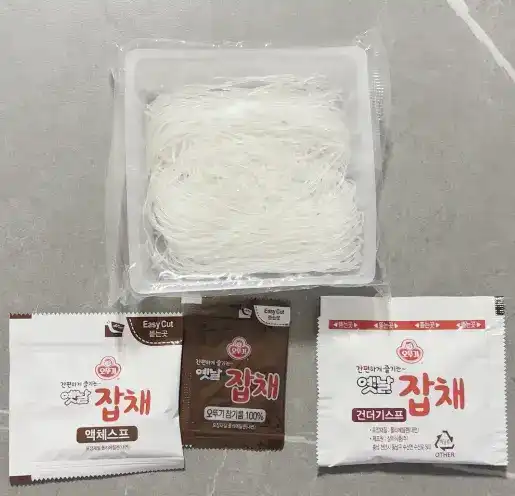 Inside look of Ottogi Japchae showing the dry glass noodles and vegetable flakes before cooking