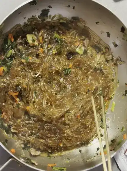 Close-up shot of thin, translucent Korean glass noodles being lifted with chopsticks