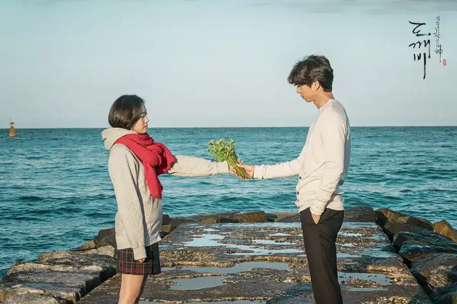 The iconic romantic scene at Jumunjin breakwater featuring Ji Eun-tak wearing her signature red scarf receiving flowers from the Goblin